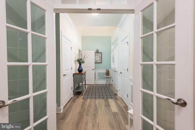 corridor featuring wainscoting, wood finished floors, crown molding, french doors, and a decorative wall