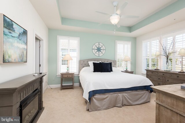 bedroom with a fireplace, a raised ceiling, light colored carpet, ceiling fan, and baseboards