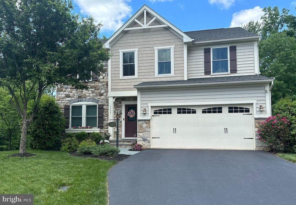 craftsman-style home featuring aphalt driveway, a front yard, stone siding, and an attached garage