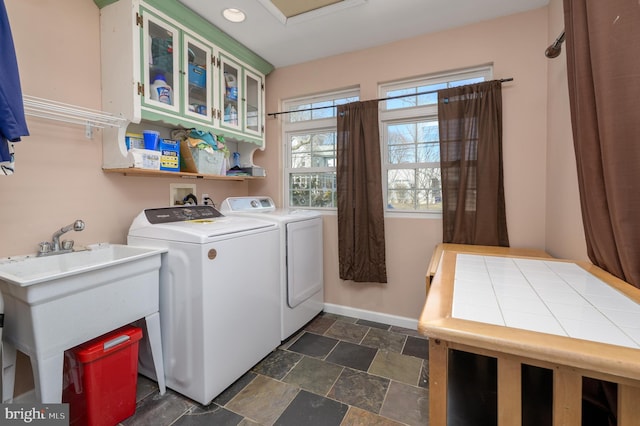 laundry area with baseboards, cabinet space, a sink, stone finish floor, and washer and dryer