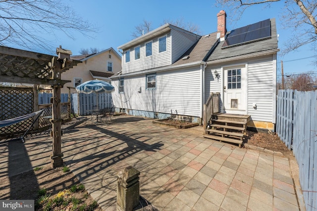 rear view of property featuring a patio area, solar panels, a chimney, and fence