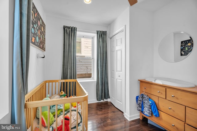 bedroom with a closet, baseboards, a nursery area, and dark wood-style flooring