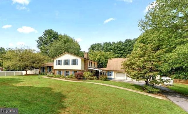 tri-level home with an attached garage, a chimney, fence, and a front yard