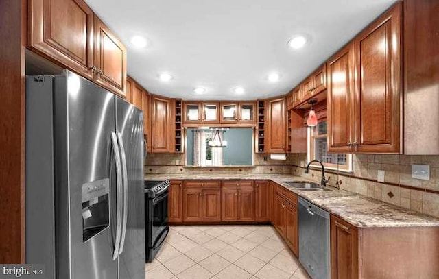 kitchen with light stone counters, appliances with stainless steel finishes, brown cabinetry, light tile patterned flooring, and a sink