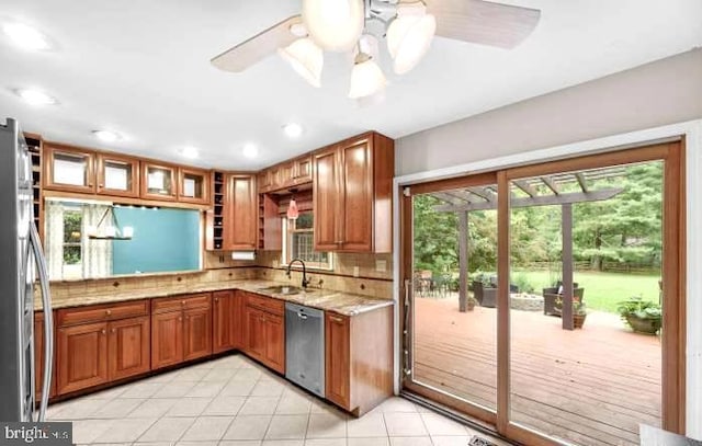 kitchen with light stone counters, stainless steel appliances, tasteful backsplash, brown cabinetry, and a sink