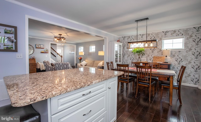 kitchen with dark wood finished floors, white cabinetry, crown molding, wallpapered walls, and light stone countertops