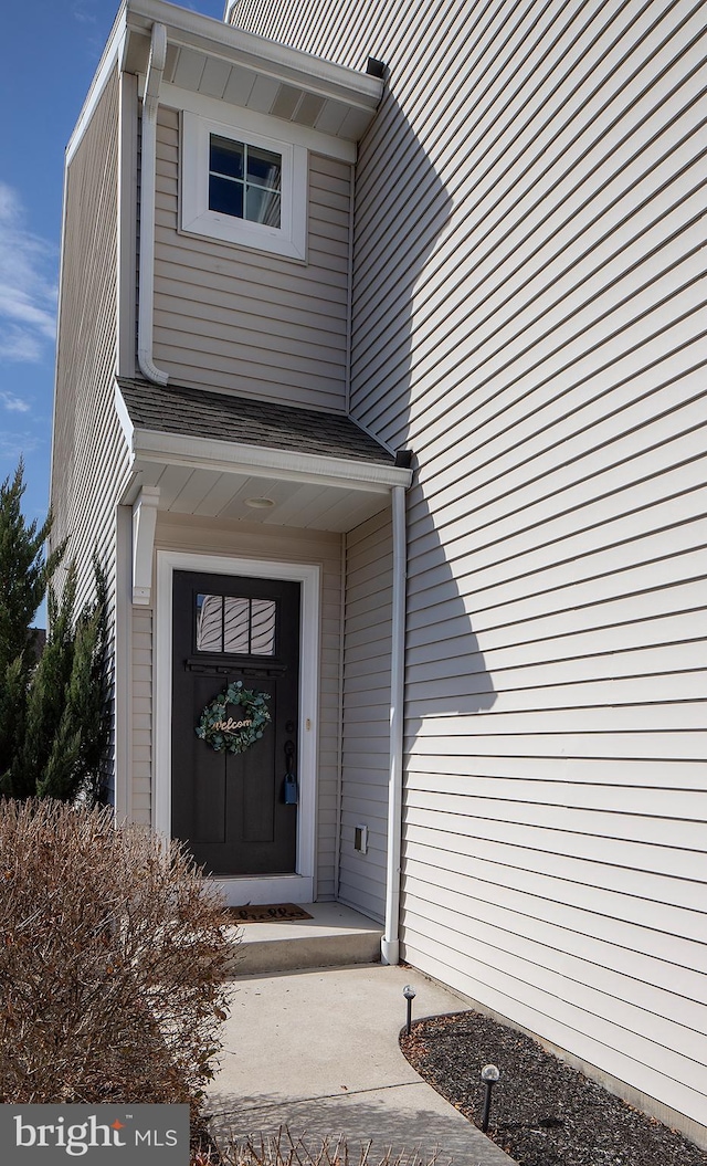 doorway to property featuring roof with shingles