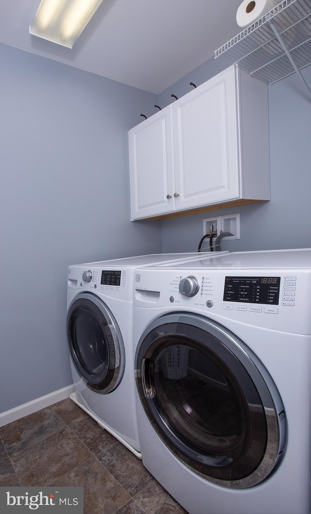 clothes washing area featuring washing machine and dryer, cabinet space, and baseboards