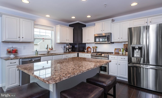 kitchen featuring a kitchen bar, ornamental molding, a sink, dark wood finished floors, and stainless steel appliances