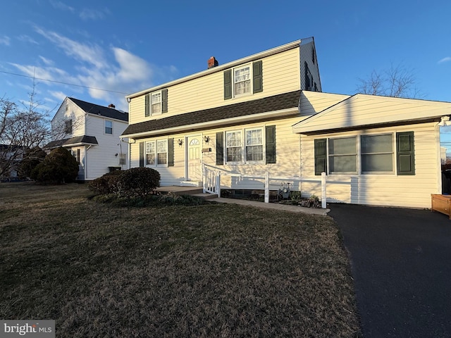 view of front of home featuring a shingled roof, a front yard, and a chimney