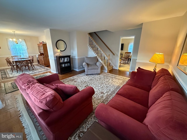 living room featuring a notable chandelier, stairway, baseboards, and wood finished floors