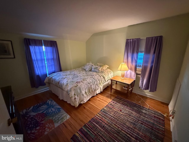 bedroom with vaulted ceiling, wood finished floors, and baseboards