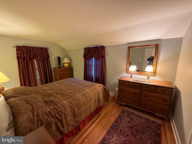 bedroom featuring baseboards, lofted ceiling, and light wood finished floors