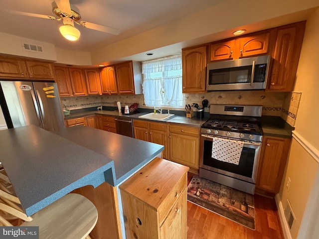 kitchen featuring visible vents, brown cabinets, a sink, dark countertops, and appliances with stainless steel finishes