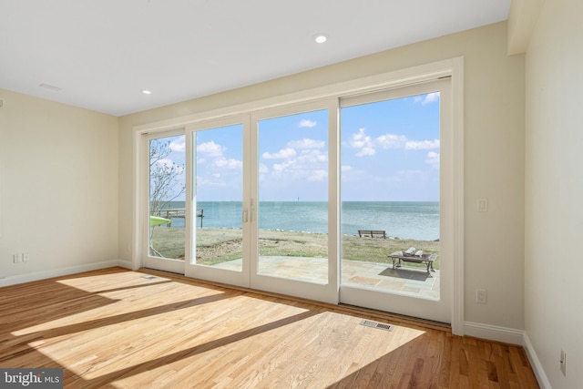 doorway featuring baseboards, visible vents, wood finished floors, a water view, and recessed lighting