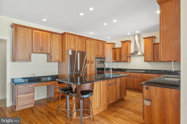 kitchen featuring light wood-style floors, an island with sink, appliances with stainless steel finishes, wall chimney range hood, and a sink