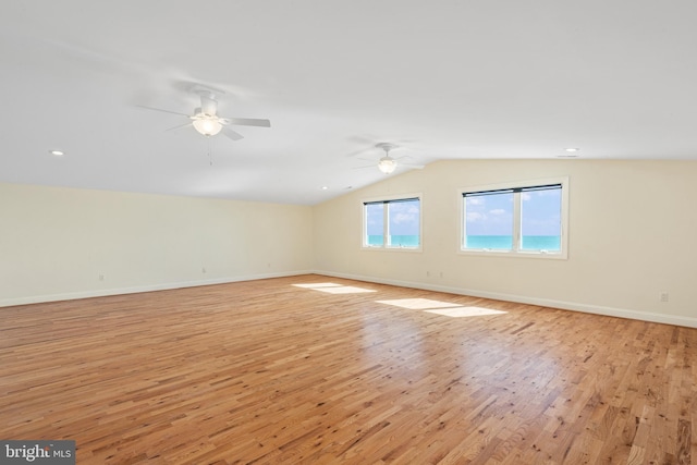 spare room with a ceiling fan, lofted ceiling, light wood-style flooring, and baseboards