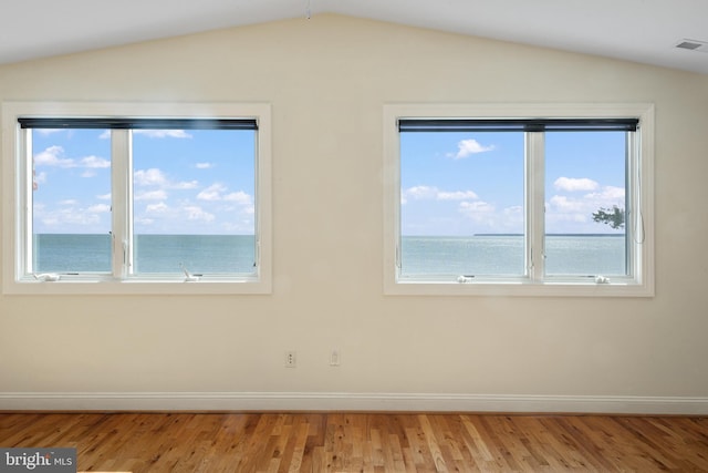 unfurnished room with visible vents, baseboards, lofted ceiling, light wood-style flooring, and a water view