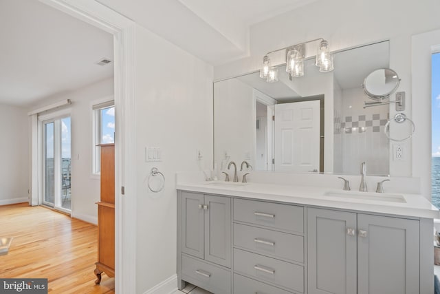 full bath with double vanity, a sink, baseboards, and wood finished floors