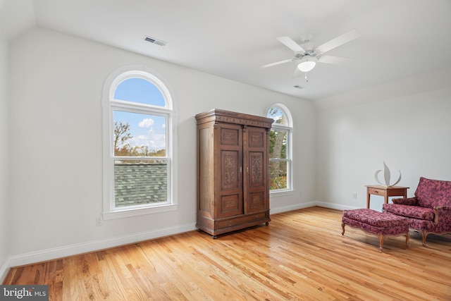 living area featuring baseboards, visible vents, vaulted ceiling, and light wood finished floors