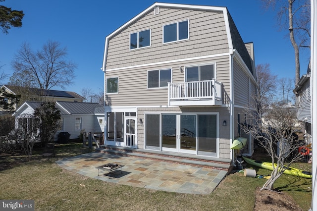 back of house featuring a balcony, a gambrel roof, a lawn, and a patio