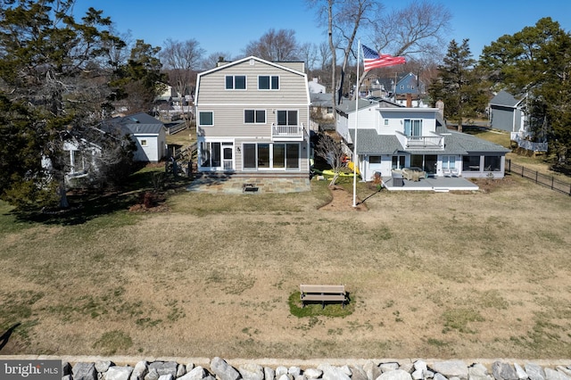 rear view of property with a balcony, fence, a gambrel roof, a lawn, and a patio area