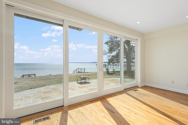 doorway to outside featuring a water view, baseboards, visible vents, and wood finished floors