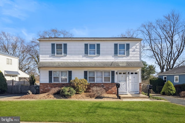 view of front of property with a front lawn, fence, brick siding, and a shingled roof