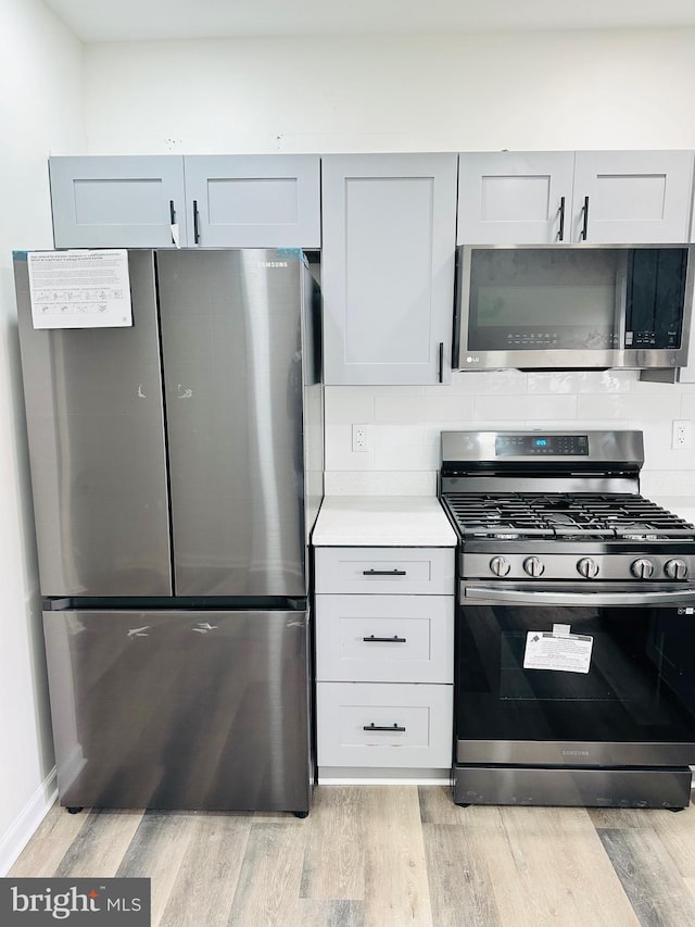 kitchen featuring stainless steel appliances, light wood-type flooring, light countertops, and decorative backsplash