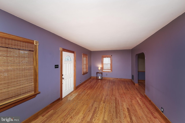 entryway with light wood-type flooring, arched walkways, and baseboards