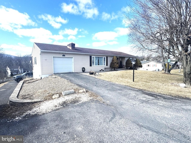 ranch-style home with driveway, an attached garage, a chimney, and a front yard