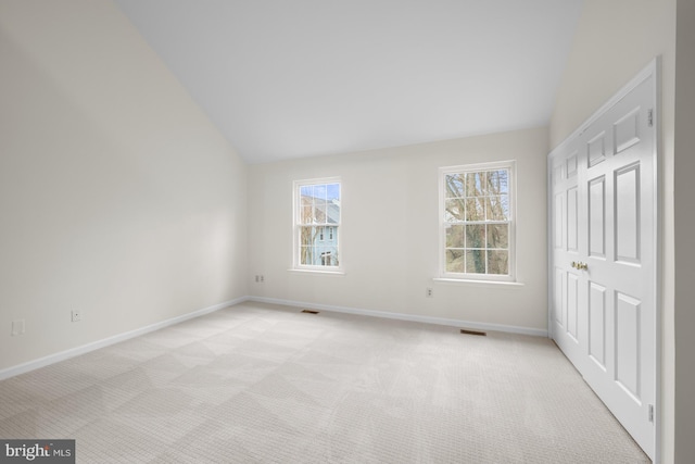 unfurnished room with light carpet, visible vents, baseboards, and vaulted ceiling