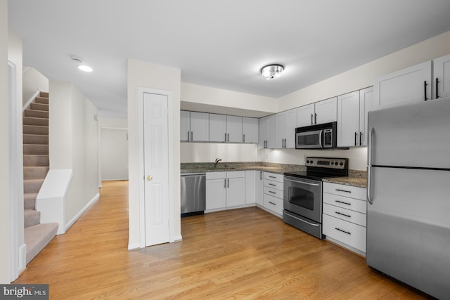 kitchen featuring stainless steel appliances, dark stone countertops, a sink, and light wood-style floors