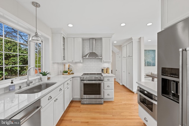 kitchen with a sink, stainless steel appliances, white cabinetry, wall chimney range hood, and tasteful backsplash