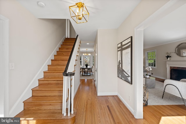 stairway with a notable chandelier, a brick fireplace, baseboards, and wood finished floors