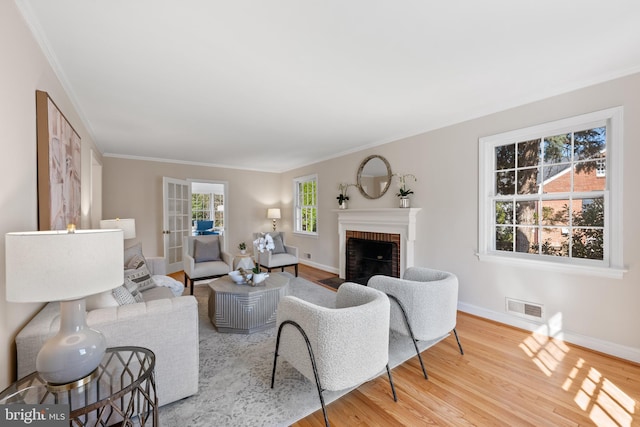 living room with visible vents, a brick fireplace, crown molding, baseboards, and wood finished floors