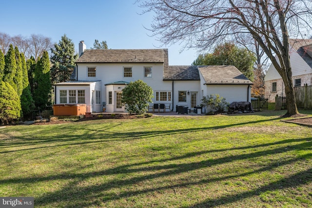 back of property with a high end roof, a hot tub, fence, a chimney, and a patio area