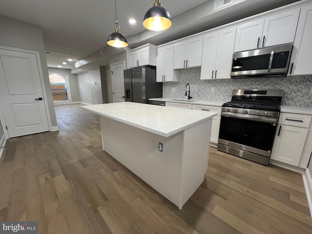 kitchen with stainless steel appliances, light countertops, a kitchen island, and wood finished floors