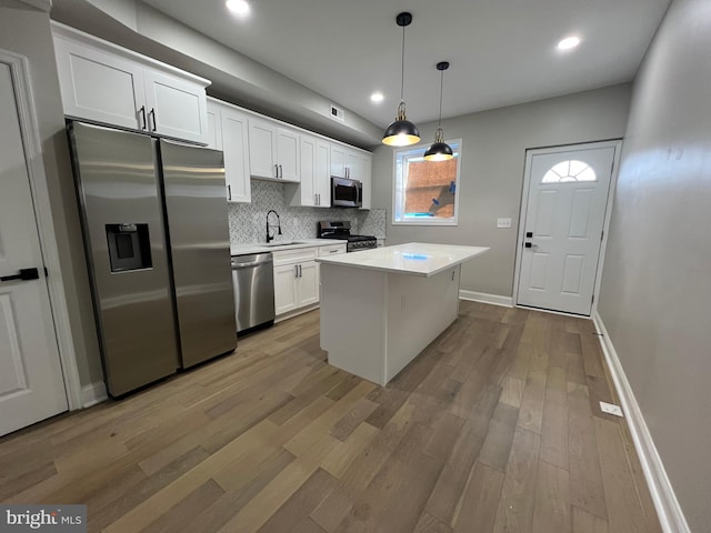 kitchen with wood finished floors, white cabinets, light countertops, appliances with stainless steel finishes, and decorative backsplash