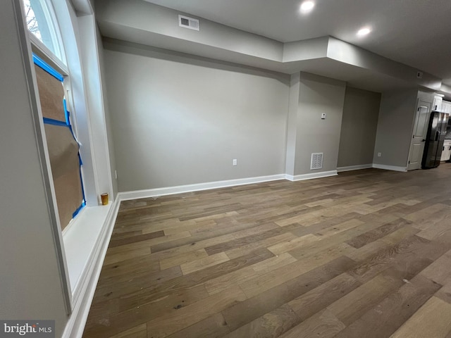 below grade area featuring visible vents, wood finished floors, freestanding refrigerator, and baseboards