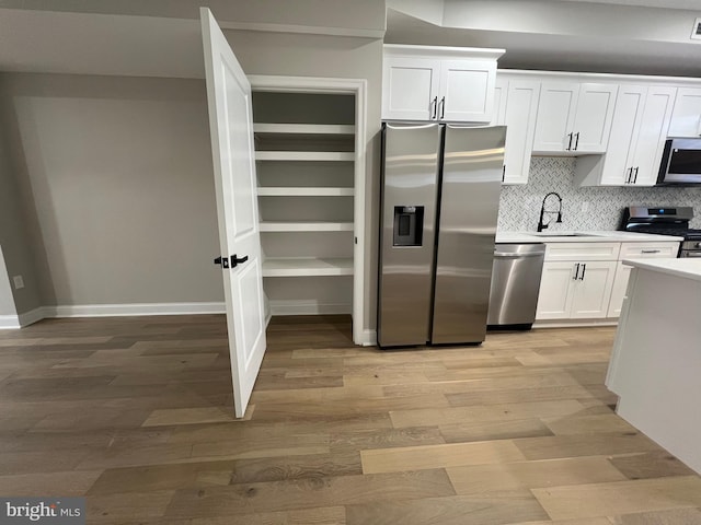 kitchen with light wood-style flooring, a sink, white cabinets, light countertops, and appliances with stainless steel finishes