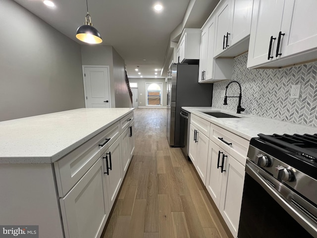 kitchen with light wood finished floors, stainless steel appliances, backsplash, white cabinetry, and a sink