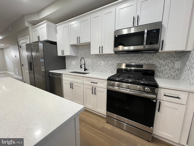 kitchen featuring tasteful backsplash, appliances with stainless steel finishes, white cabinetry, a sink, and wood finished floors