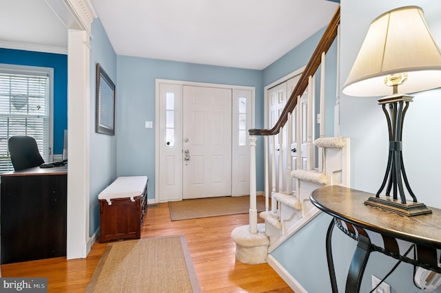 foyer entrance with stairway, baseboards, and light wood finished floors