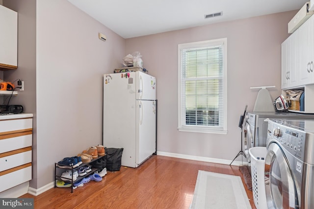 clothes washing area with light wood-type flooring, visible vents, washer and clothes dryer, cabinet space, and baseboards