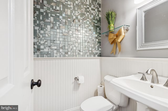 half bath featuring toilet, a wainscoted wall, and a sink