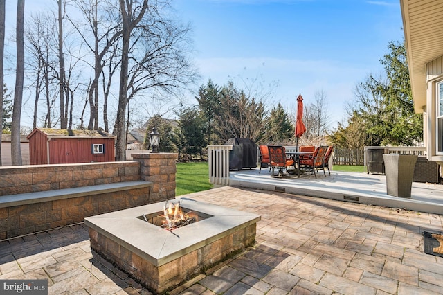 view of patio with fence, a shed, an outdoor fire pit, an outbuilding, and outdoor dining space