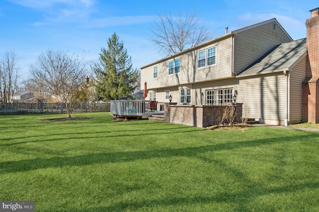 rear view of house featuring a yard, fence, a chimney, and a wooden deck