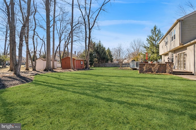 view of yard with a wooden deck, a storage unit, an outdoor structure, and fence