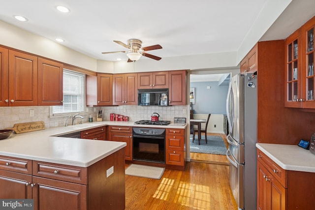 kitchen with black appliances, light wood-style flooring, a ceiling fan, a sink, and backsplash